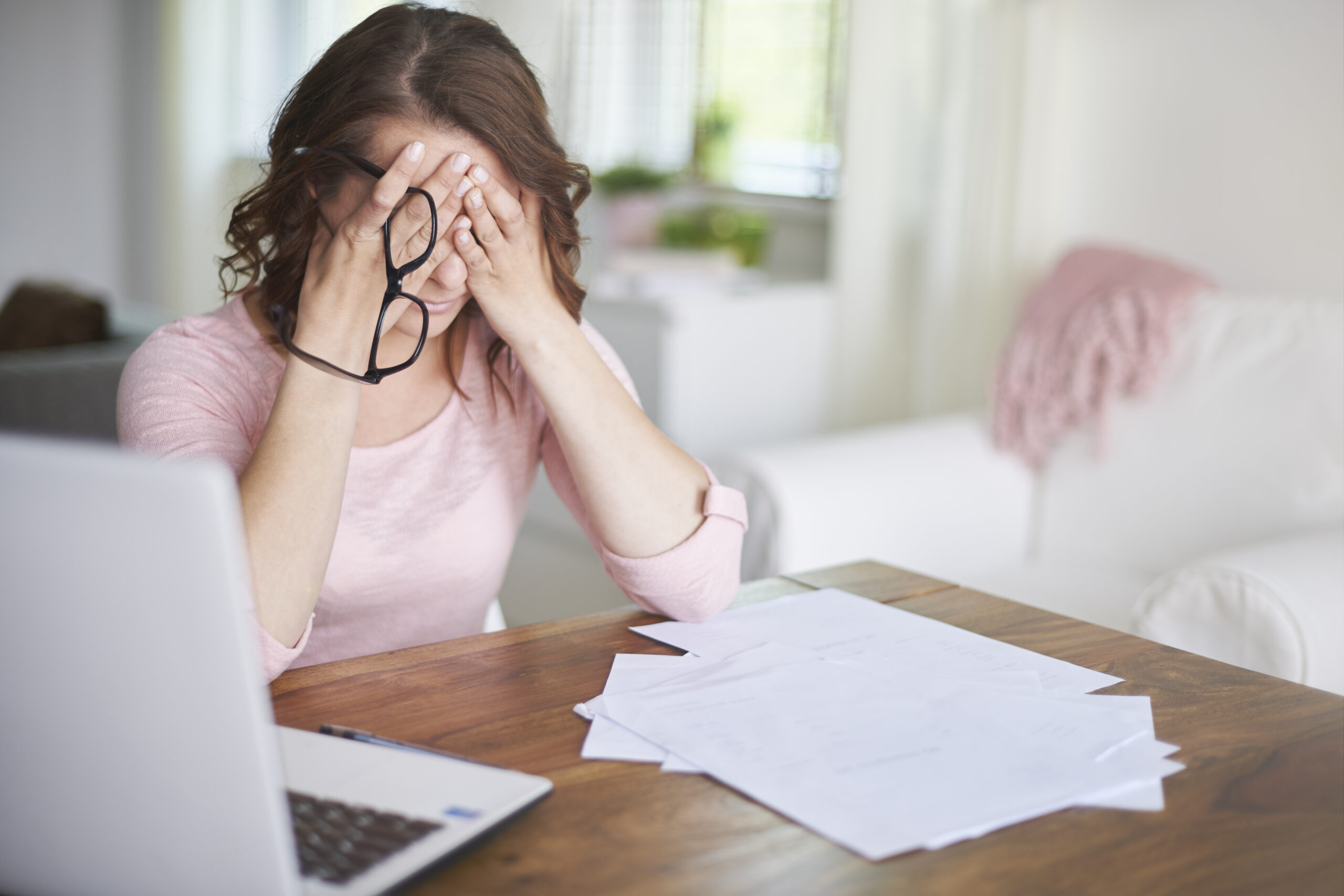 Woman feeling very stressed at her desk, laptop and paperwork in front of her